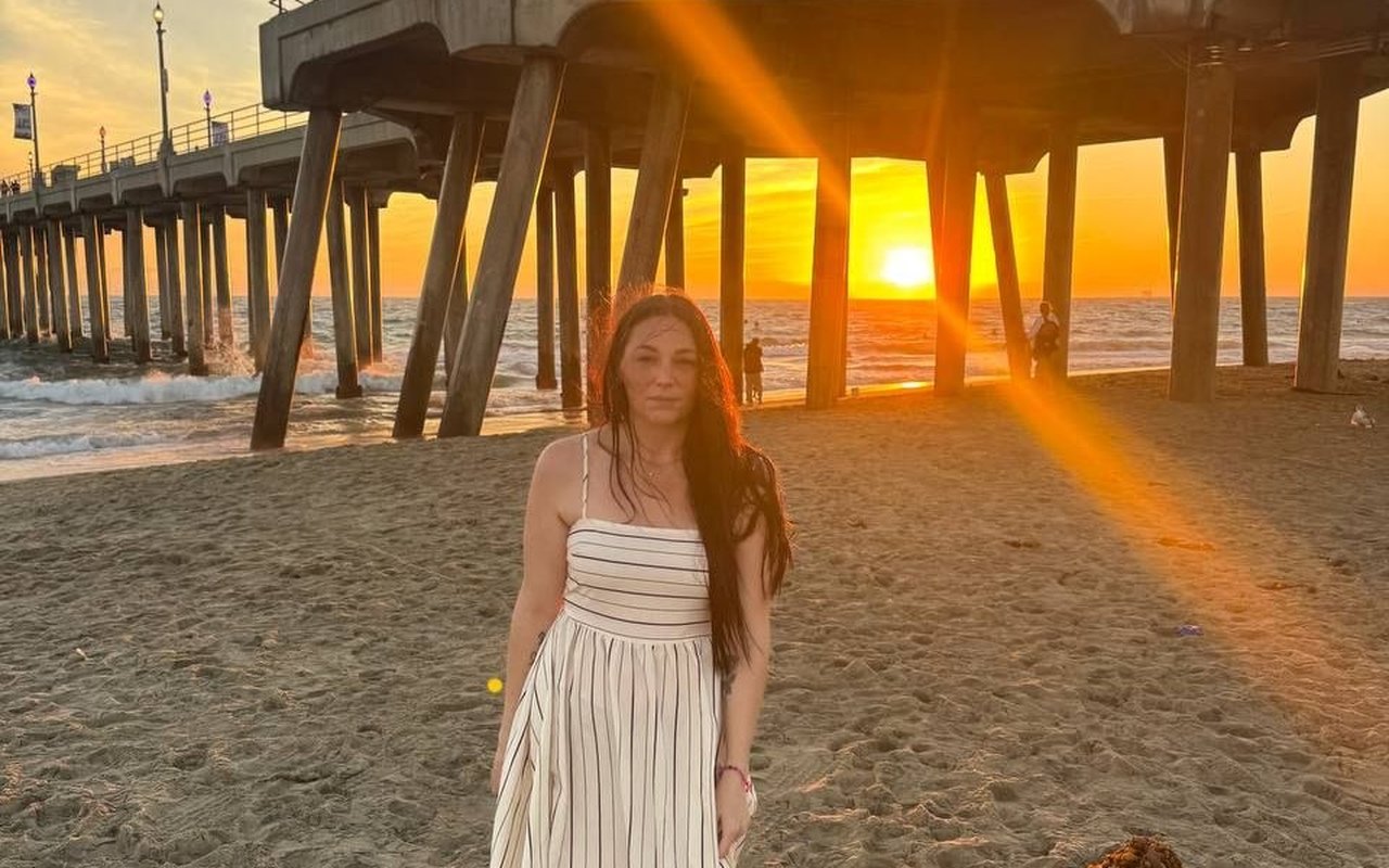 Kay standing under the pier at sunset