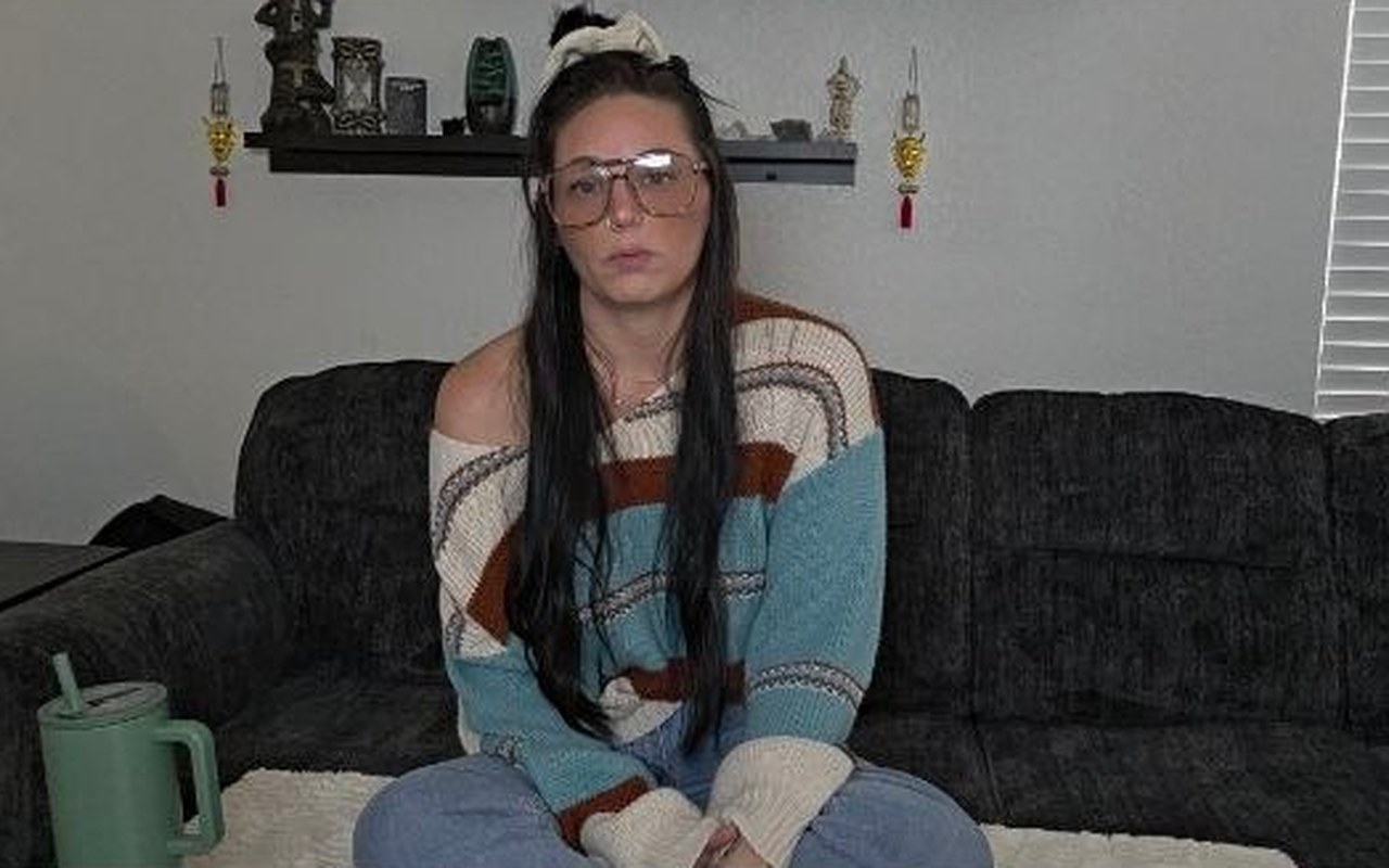 Kay on the couch mid-sentence, hoodie half off, mic in hand