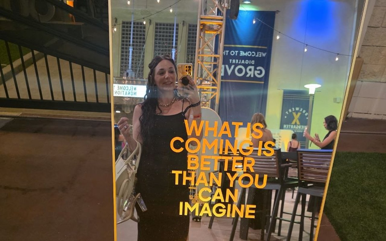 Mirror selfie; the sign in the glass reads What is coming is better than you can imagine